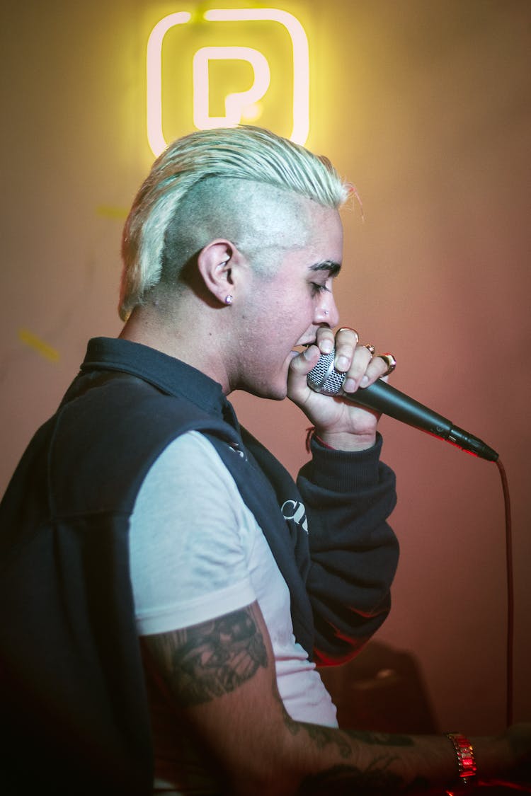 Young Man With Blonde Mohawk Hair Singing In Microphone