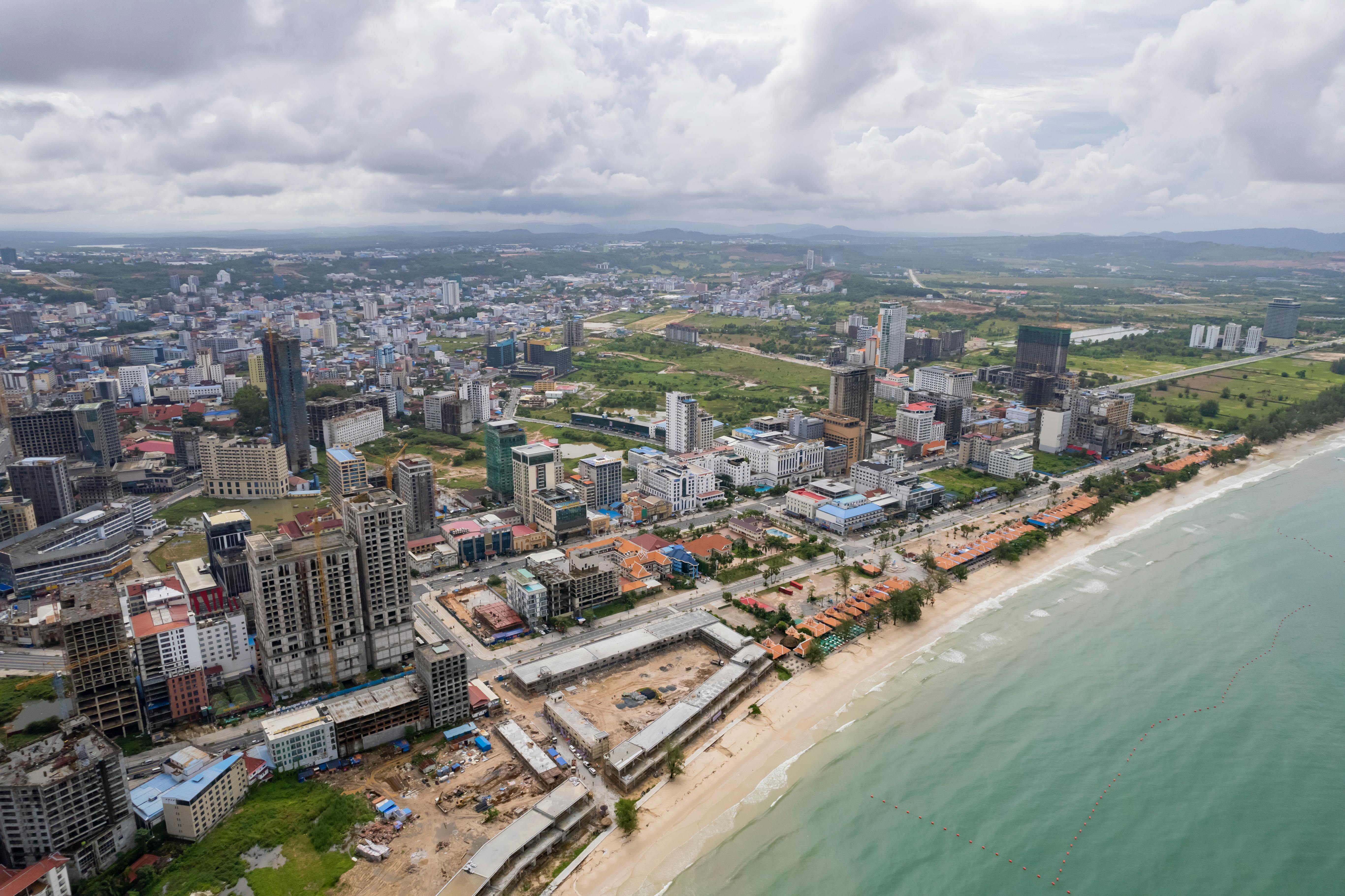 Vista aérea de uma cidade costeira com edifícios comerciais e uma praia, representando o urbanismo e o desenvolvimento urbano na proximidade ao mar.