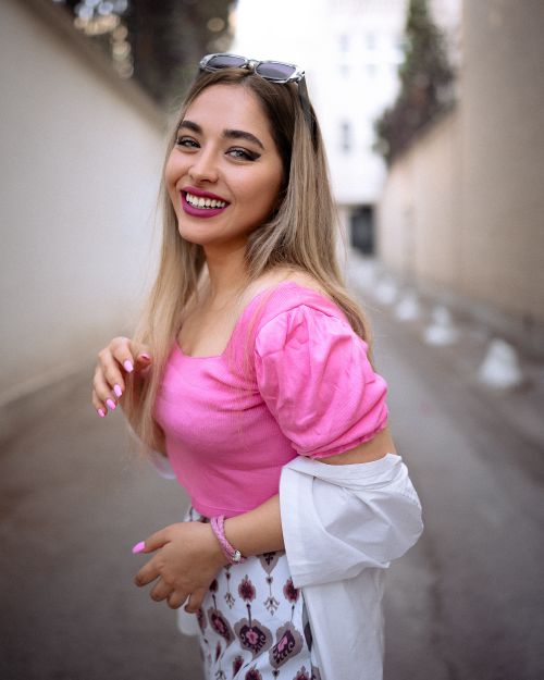 Free A woman in a pink blouse smiles on a city street, exuding vibrant fashion and urban style. Stock Photo