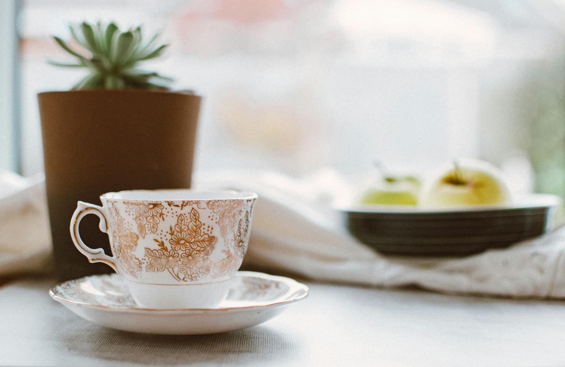 Vit och brun Floral Ceramic Teacup på vit keramisk tallrik nära brun kruka