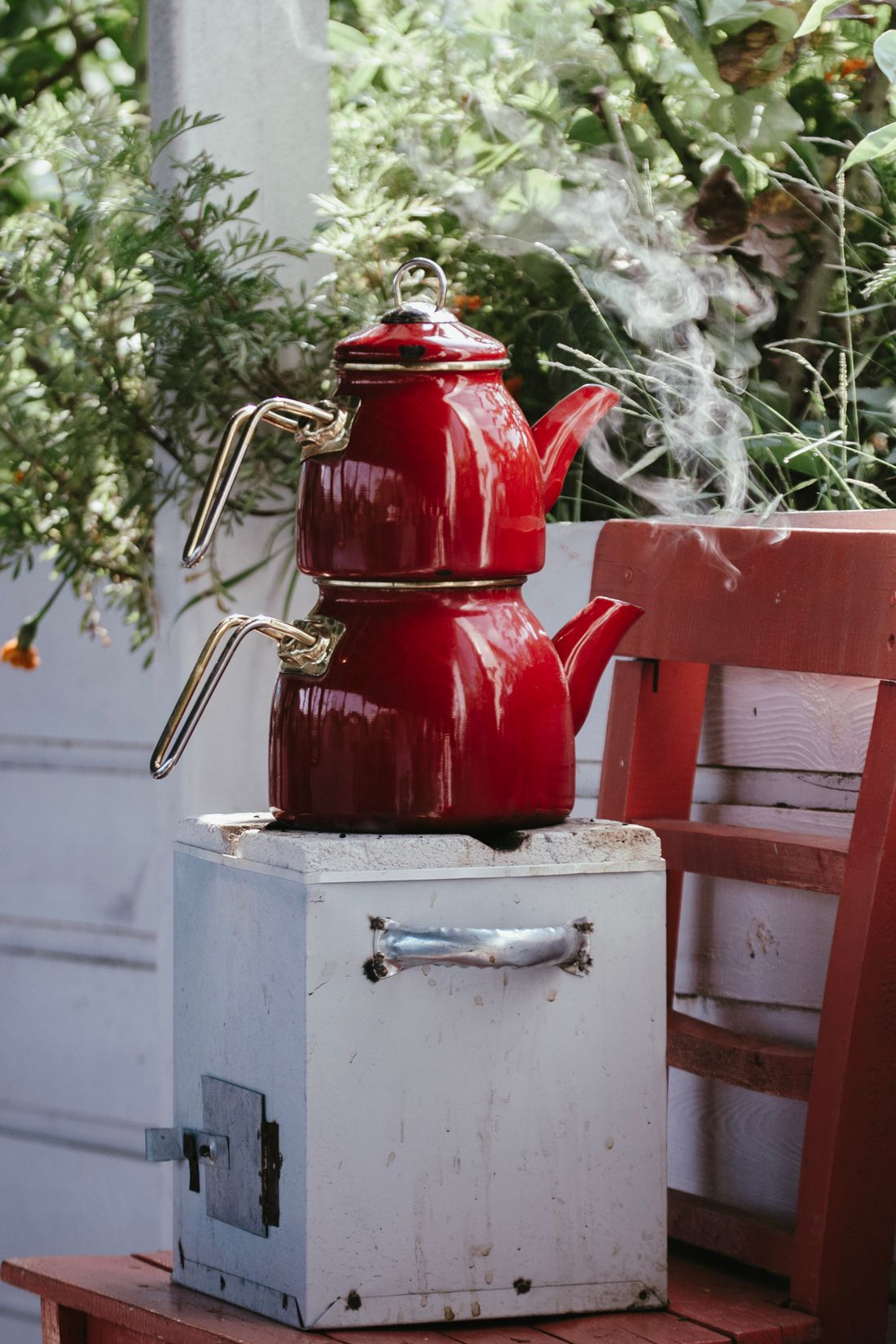 Red enamel stacked double tea kettle steaming on a white stove box