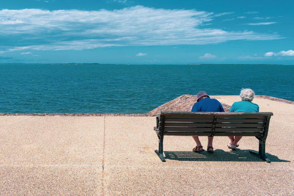Senior couple relaxing on a seaside bench, enjoying a sunny summer day overlooking the ocean.