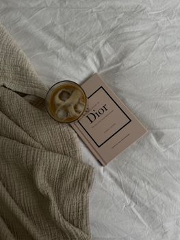 Minimalist flat lay of coffee and a Dior book on a textured bedspread.
