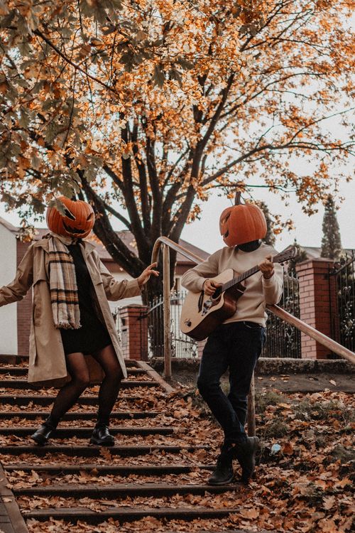 Free Creative fall photograph of two people in pumpkin masks on stairs, enjoying a seasonal moment. Stock Photo