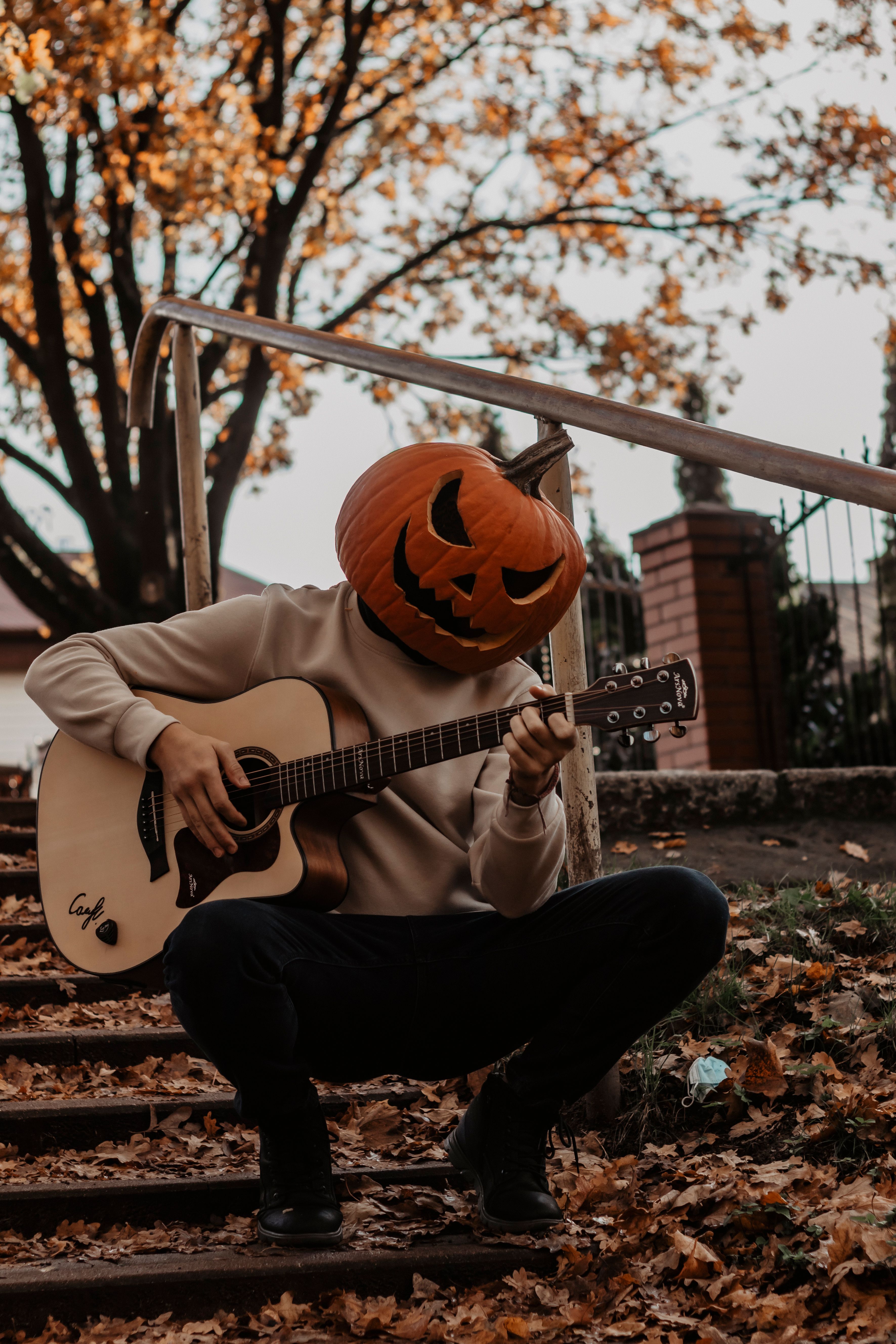 A person wearing a pumpkin head playing guitar outdoors during fall. Perfect for Halloween themes.
