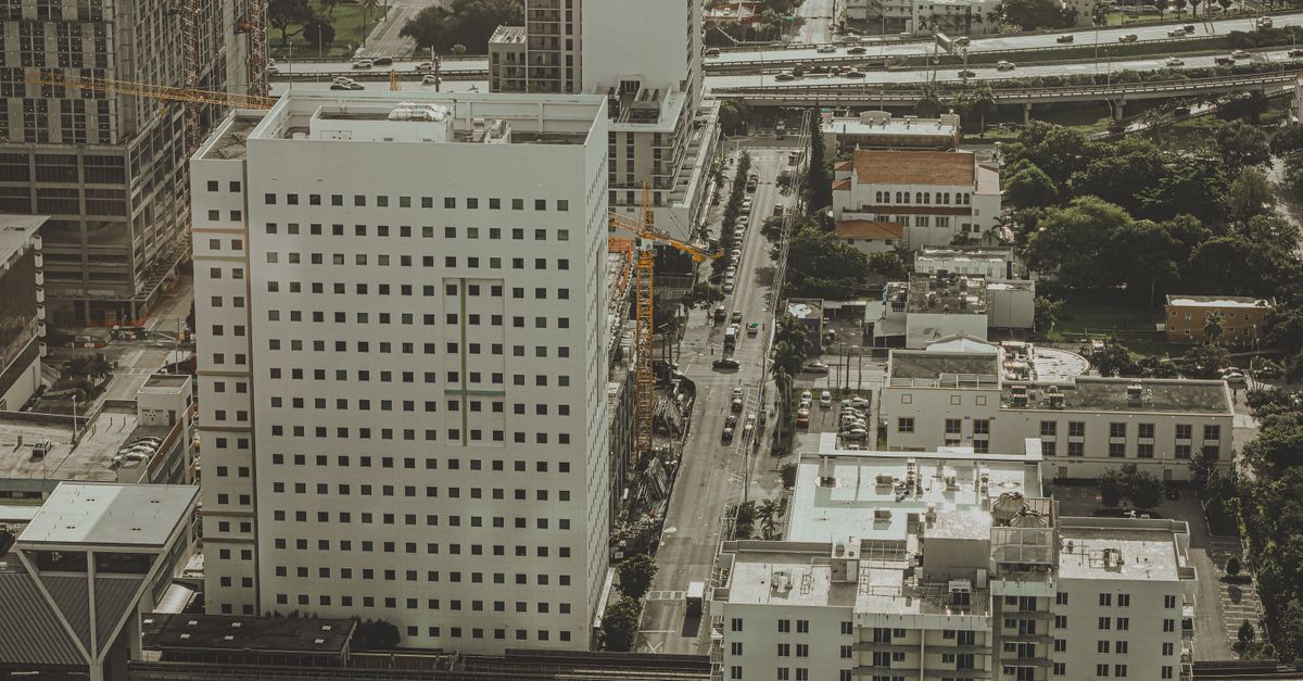 Aerial shot of city landscape with buildings, streets, and construction sites in daylight.