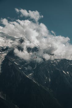 Suspended cable car amidst cloudy mountain peaks, offering a sense of adventure and exploration.