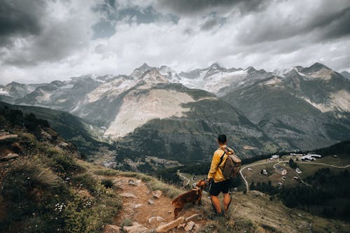 Man Standing on Trail in Mountains with Dog Overlooking Valley