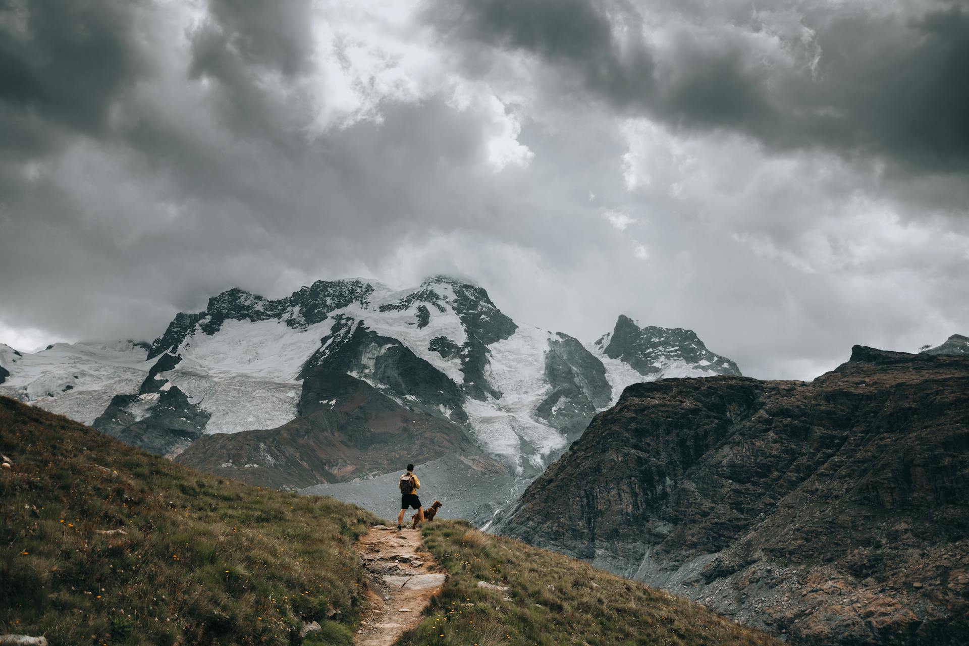 Hiker with a Dog on a Trail in the Mountains on a Cloudy Day