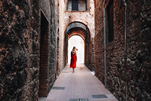 Woman in Red Dress in Narrow Alley Between Old Brick Buildings