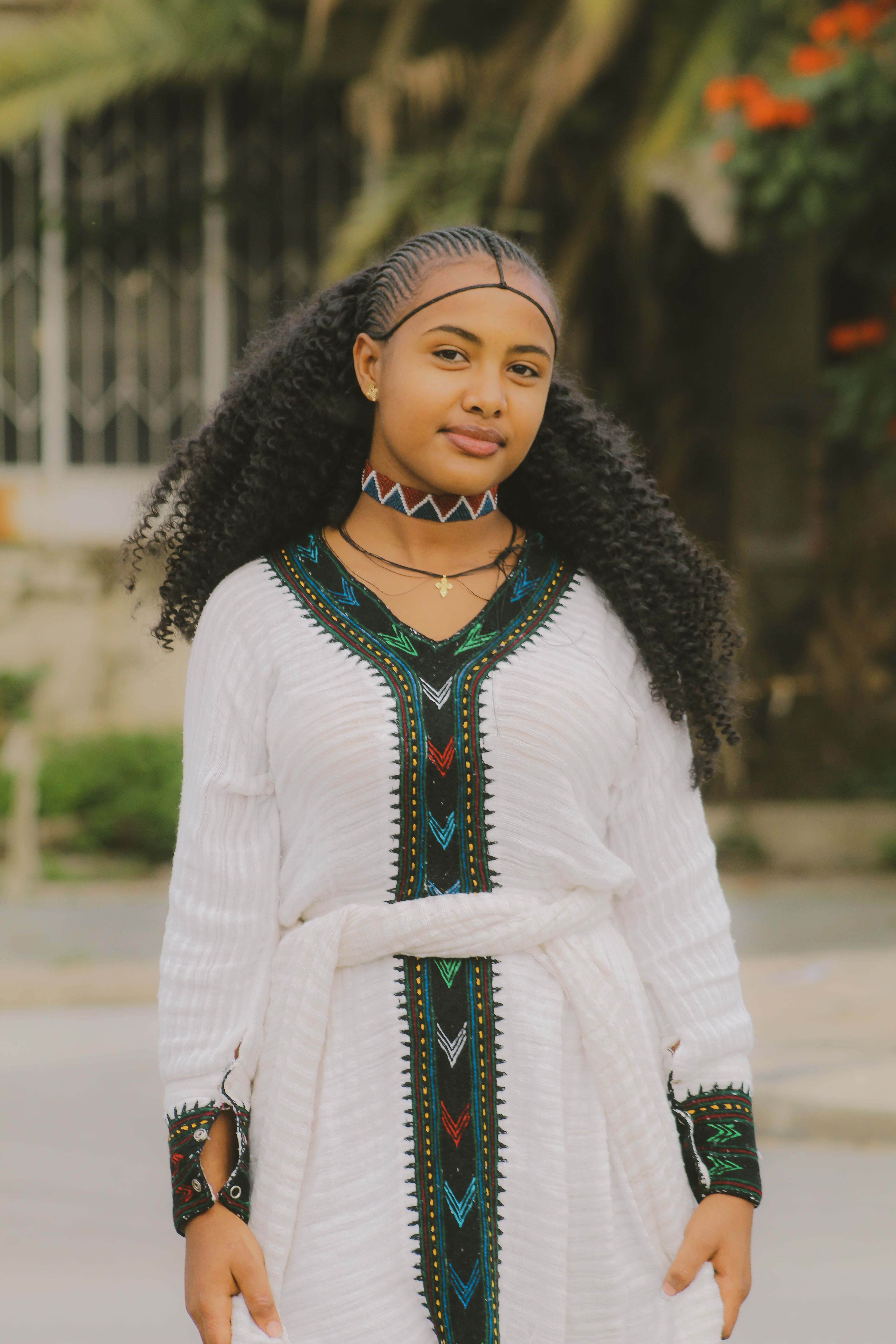 Portrait of a woman outdoors wearing a traditional white dress with intricate patterns, exuding grace and style.