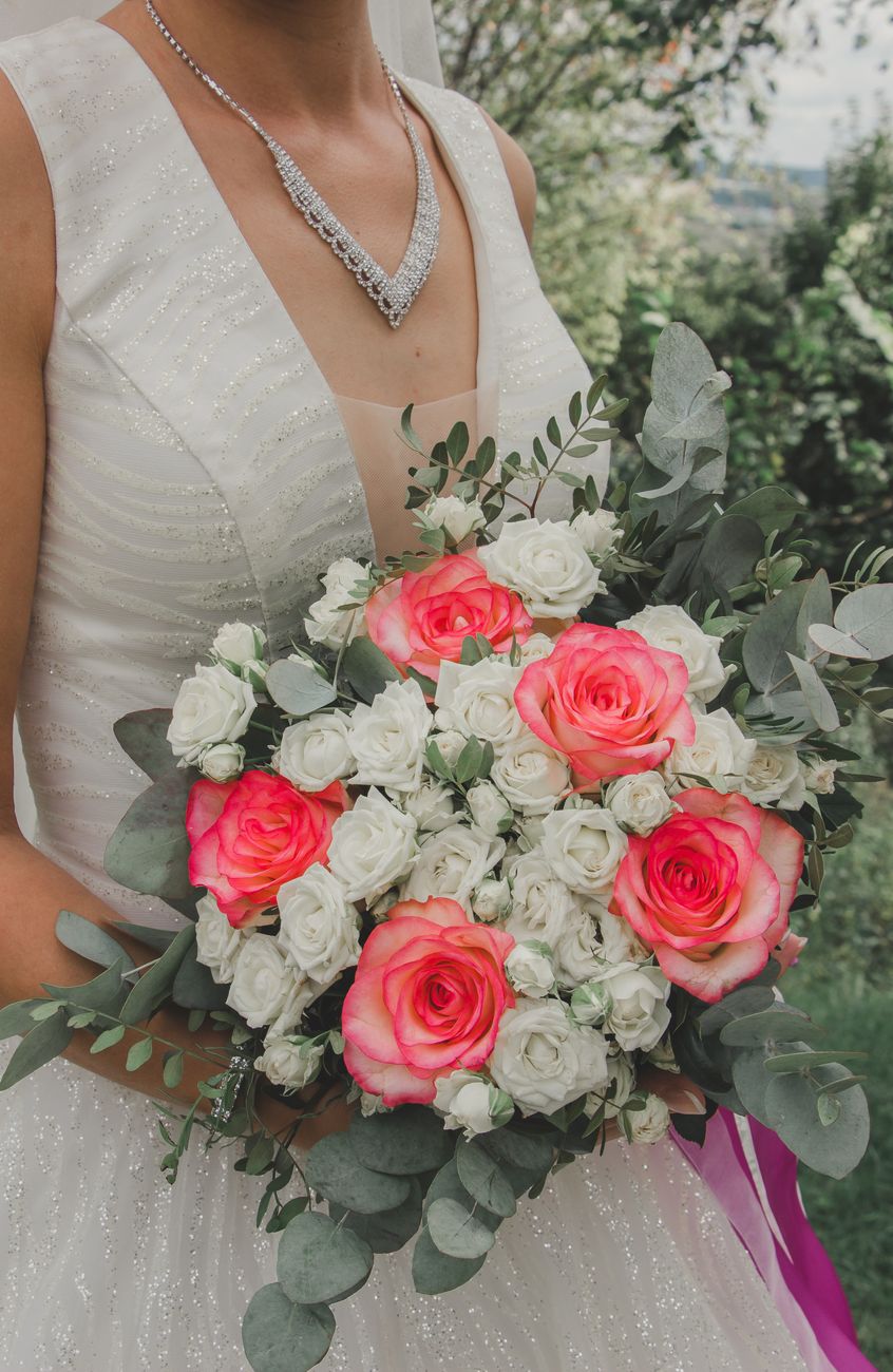 Bride in white dress holding a bouquet of pink and white roses, perfect for wedding photography.