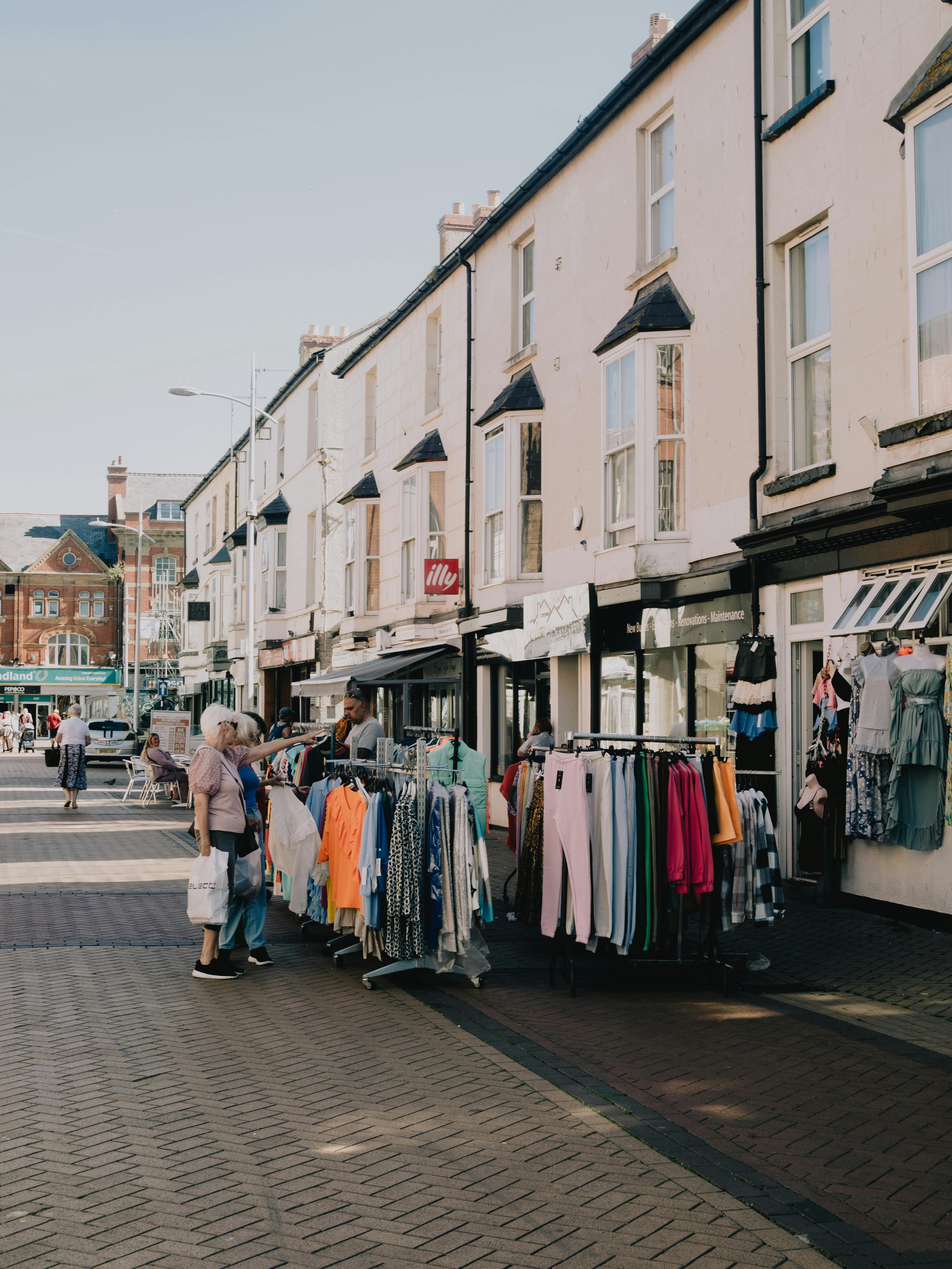 Charming street view of people browsing clothes racks on a sunny day.
