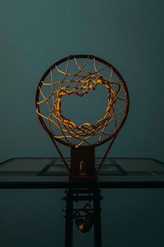 A dramatic view of a basketball hoop backlit at twilight, highlighting the net.