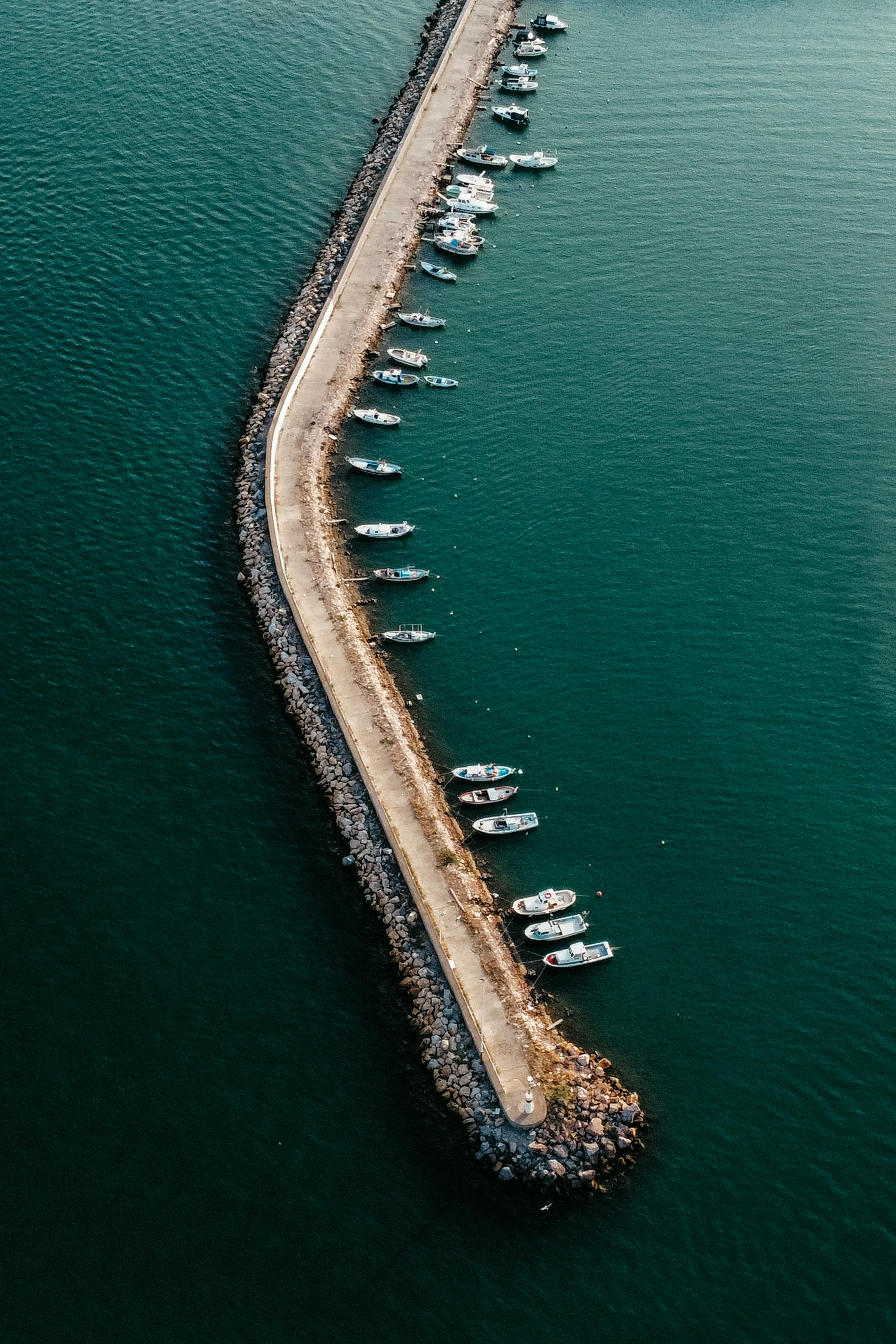Aerial photograph capturing boats moored alongside a long pier in a calm sea.