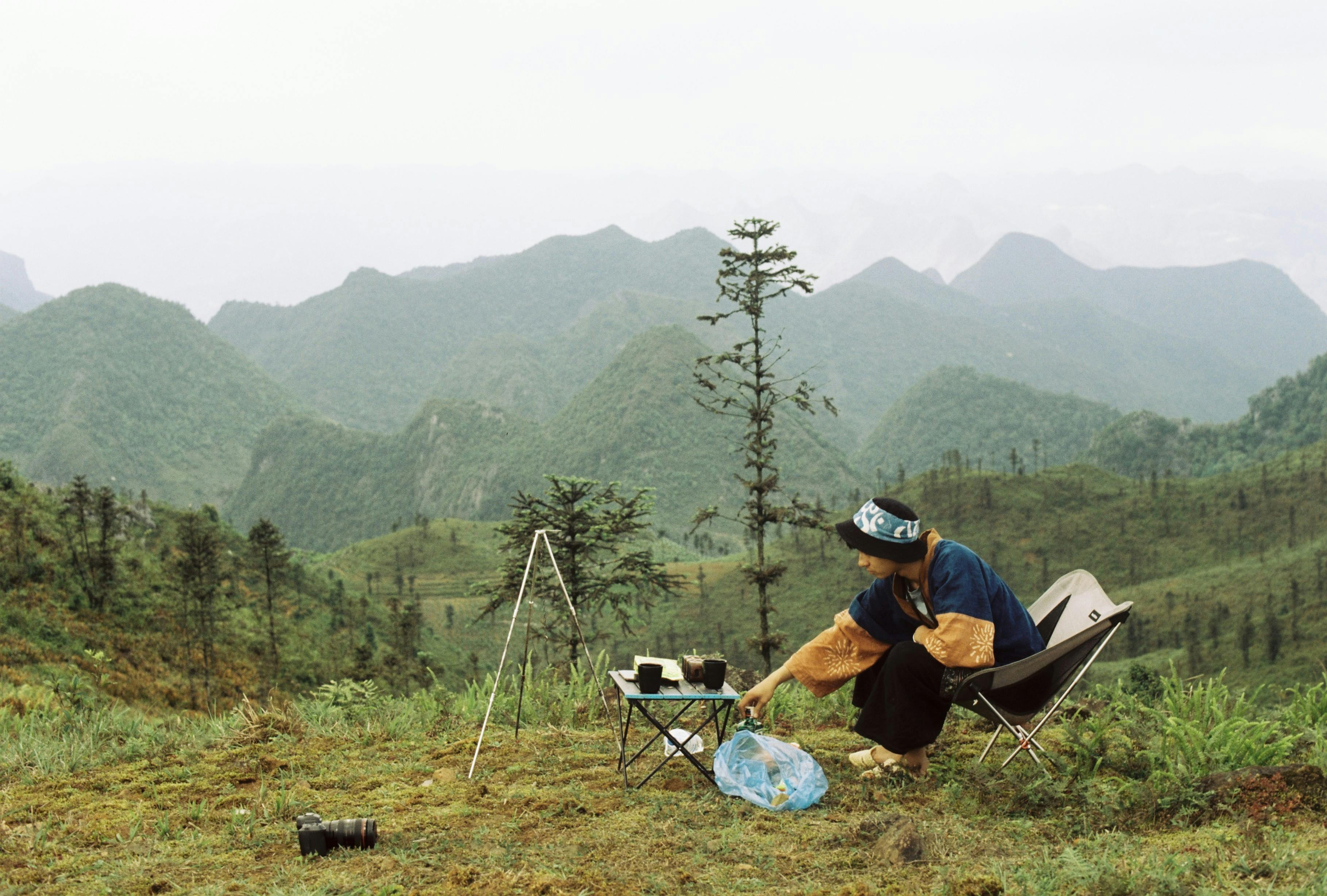 A peaceful camping scene with a person in nature, overlooking green mountains.