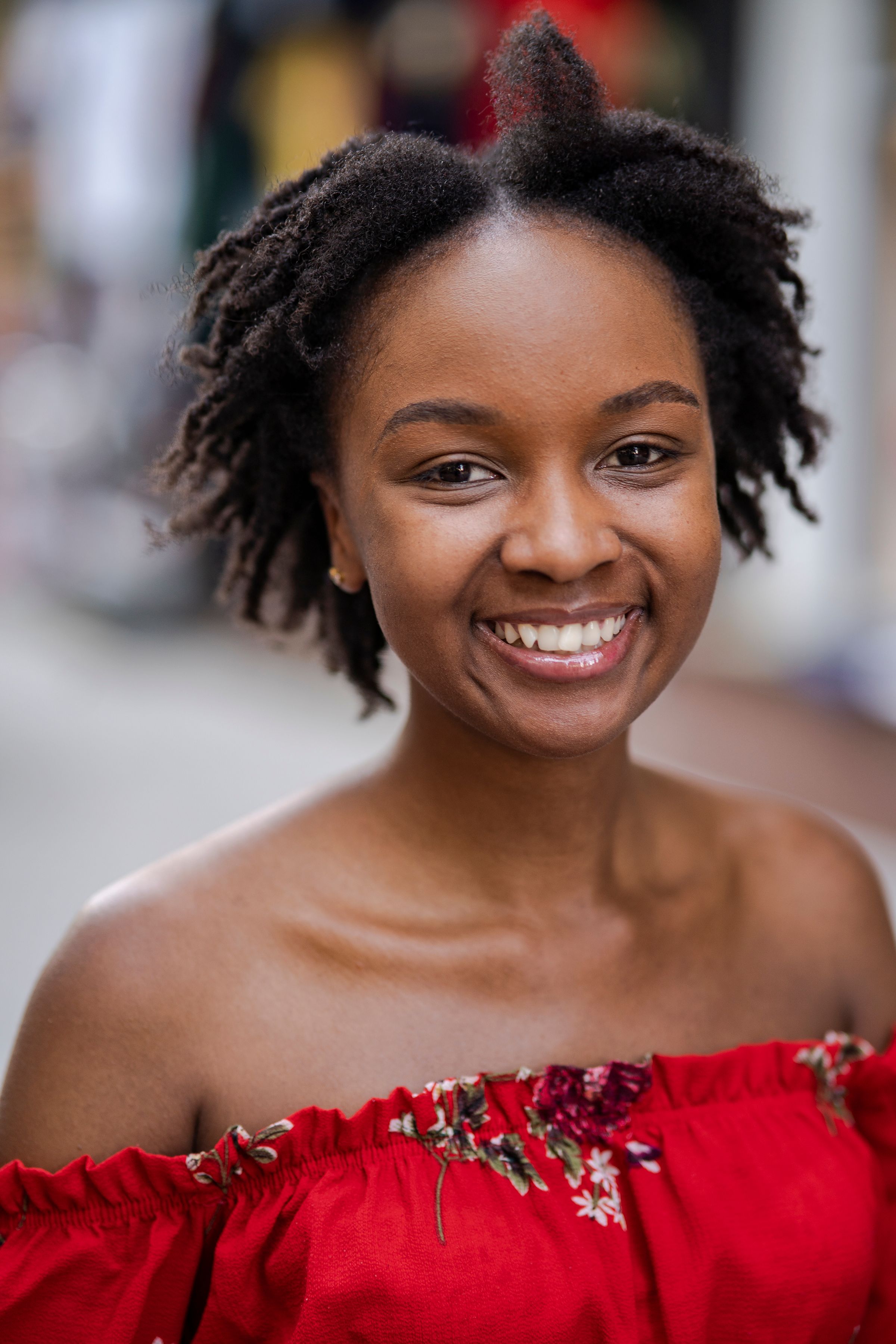 Close-up portrait of a happy woman with natural hair, wearing a red floral dress.