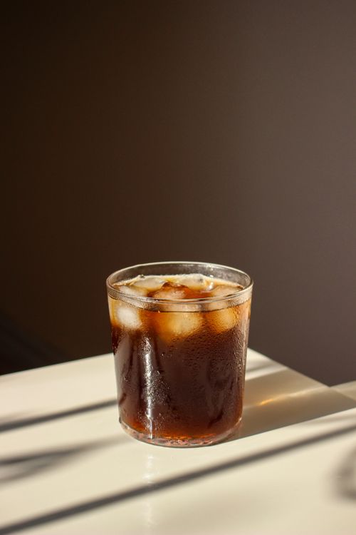 Free A chilled glass of iced coffee with ice cubes, basking in natural sunlight. Stock Photo