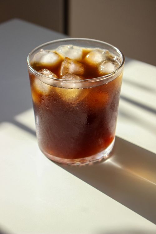Free Glass of iced coffee with ice cubes on a sunlit table, perfect for a refreshing pick-me-up. Stock Photo