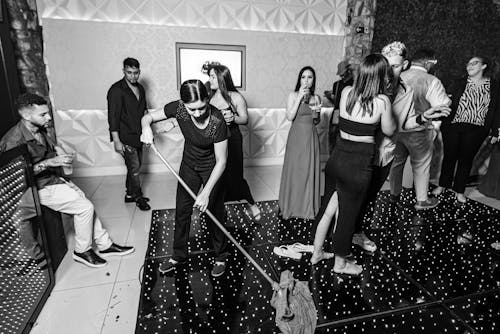 Black and White Shot of Young Woman Cleaning Floor during a Party 