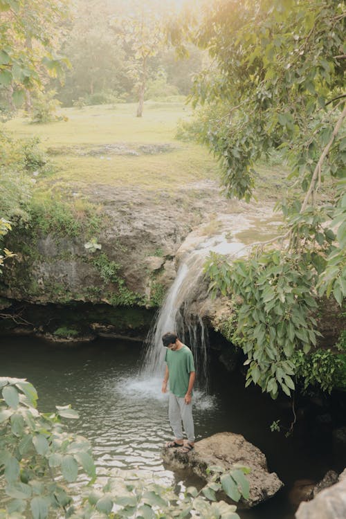 Man Standing on a Stone in a Pond Under a Waterfall