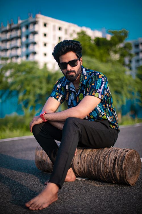Free A fashionable man sits barefoot on a log wearing sunglasses, enjoying the sunny day. Stock Photo