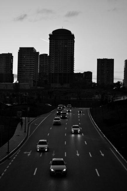 Black and white cityscape showing highway traffic at dusk against a silhouette of skyscrapers.