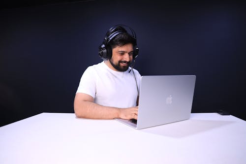 Smiling Man in Headphones with Microphone Using a Apple MacBook