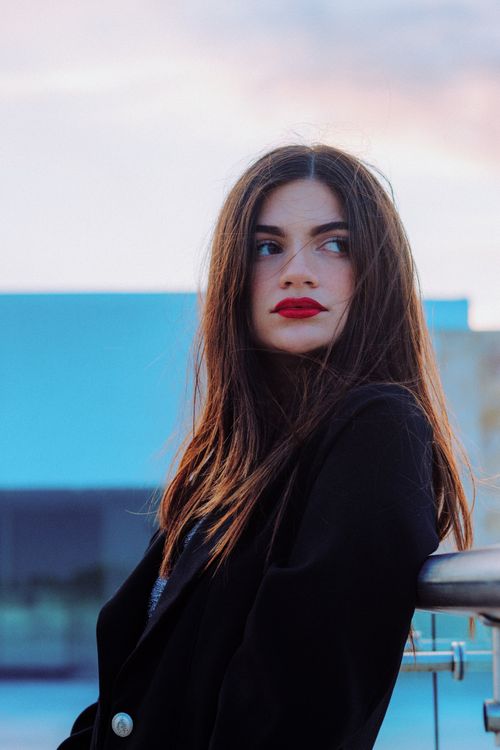 Free Portrait of a woman with red lipstick, gazing away in an outdoor setting. Stock Photo