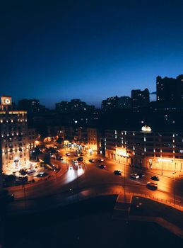 A vibrant cityscape at night featuring illuminated streets and buildings under a clear sky.