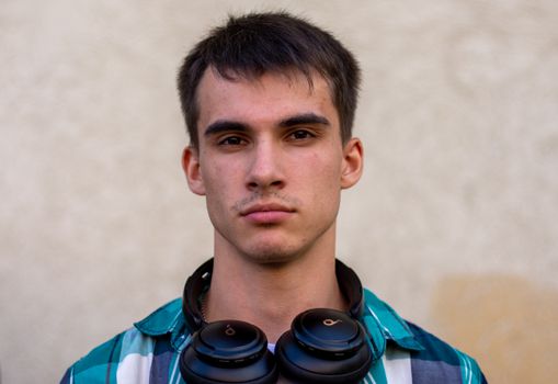 A close-up portrait of a young man wearing headphones around his neck against a neutral background.