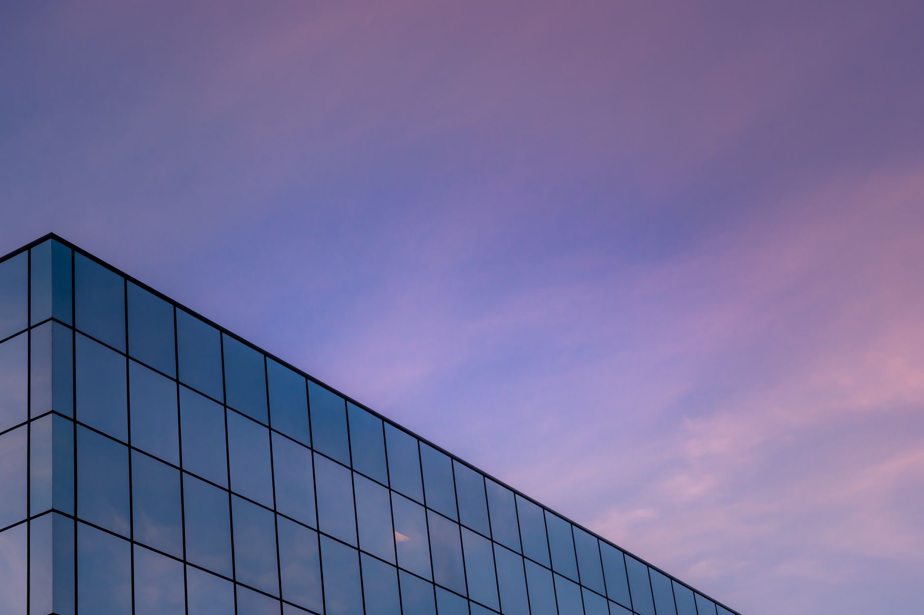 A modern glass building with a geometric design set against a serene pink sky.