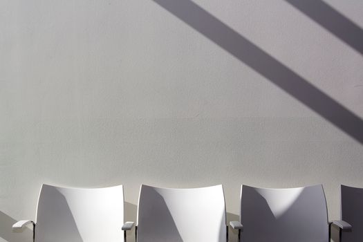 Three white chairs with long shadows against a plain wall, embodying minimalist design.