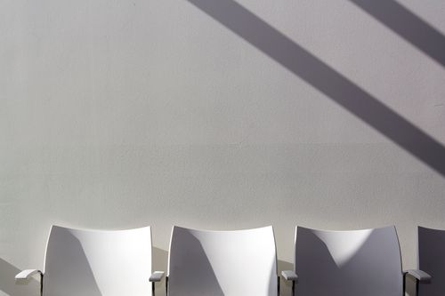 Free Three white chairs with long shadows against a plain wall, embodying minimalist design. Stock Photo