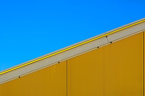 Free Minimalist architectural shot of a vivid yellow building facade contrasting with a clear blue sky. Stock Photo
