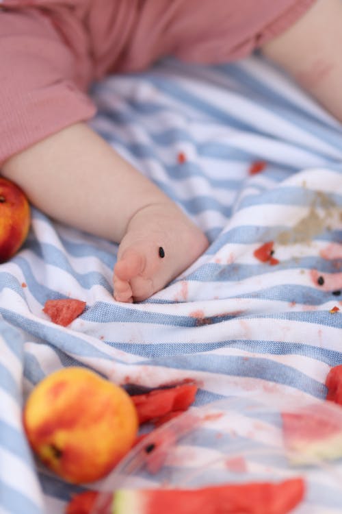 Free Barefoot Baby Lying on Blanket next to Fruits Stock Photo