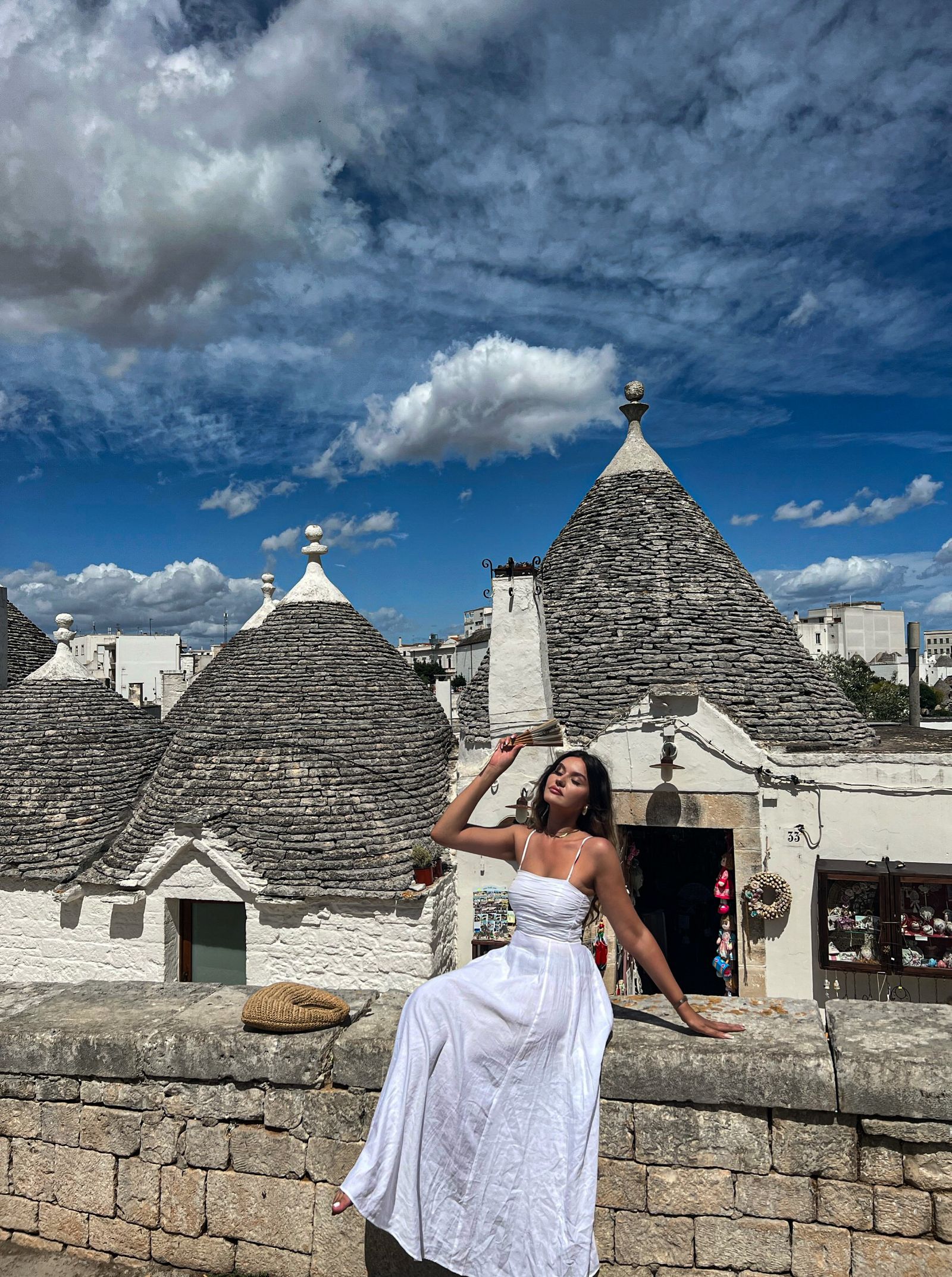 A woman in white, posing on a wall by the white trulli houses of Alberobello, Italy — the cover image of The White Edit