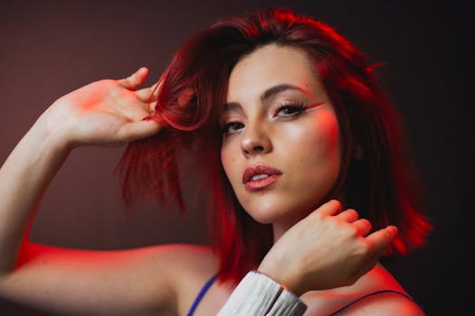 Close-up portrait of a woman with striking red hair and makeup in a moody setting.