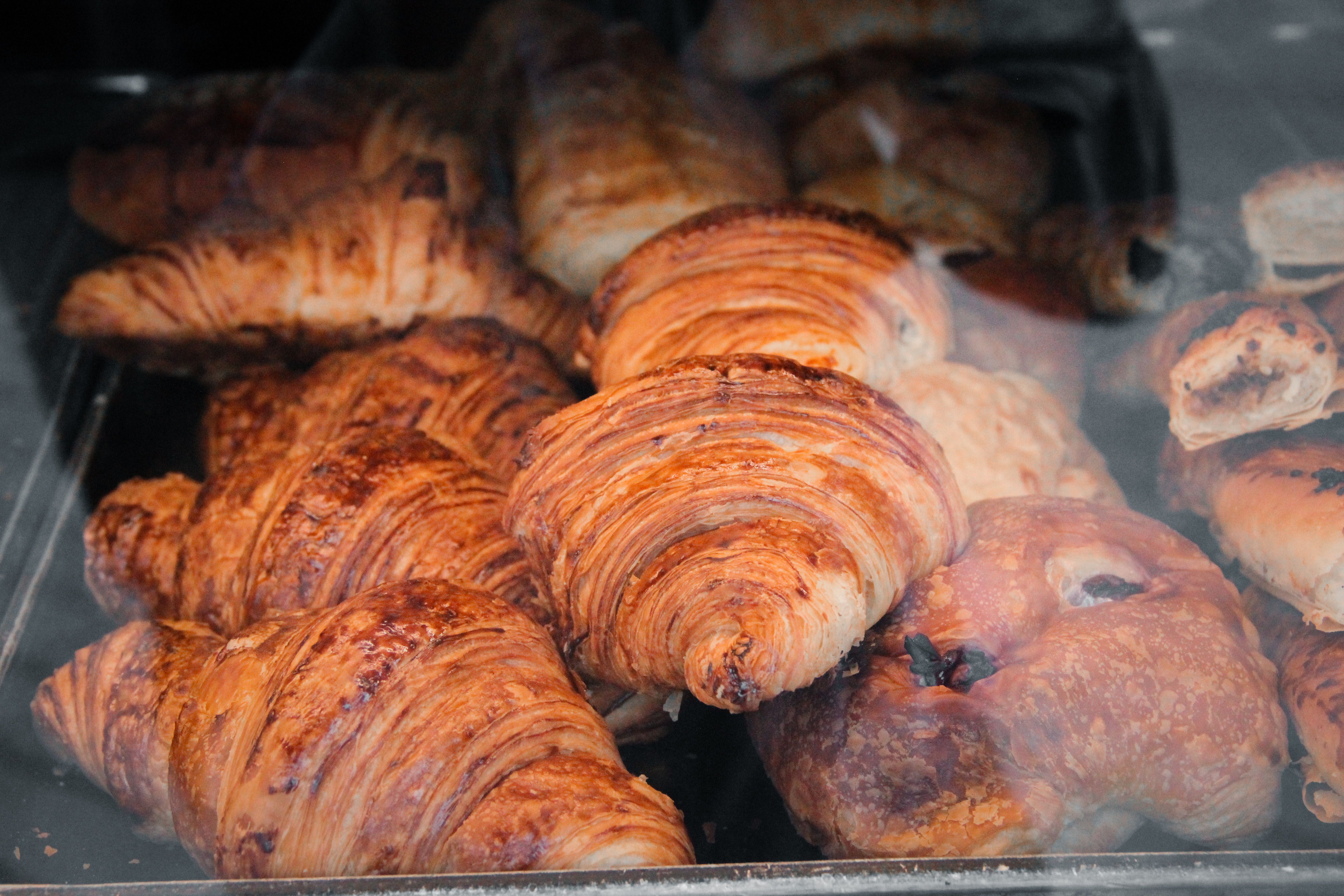 Close-up of fresh croissants and pastries displayed behind a glass in a bakery.