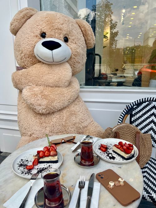 Free Giant teddy bear at a café table with strawberry desserts and tea. Stock Photo