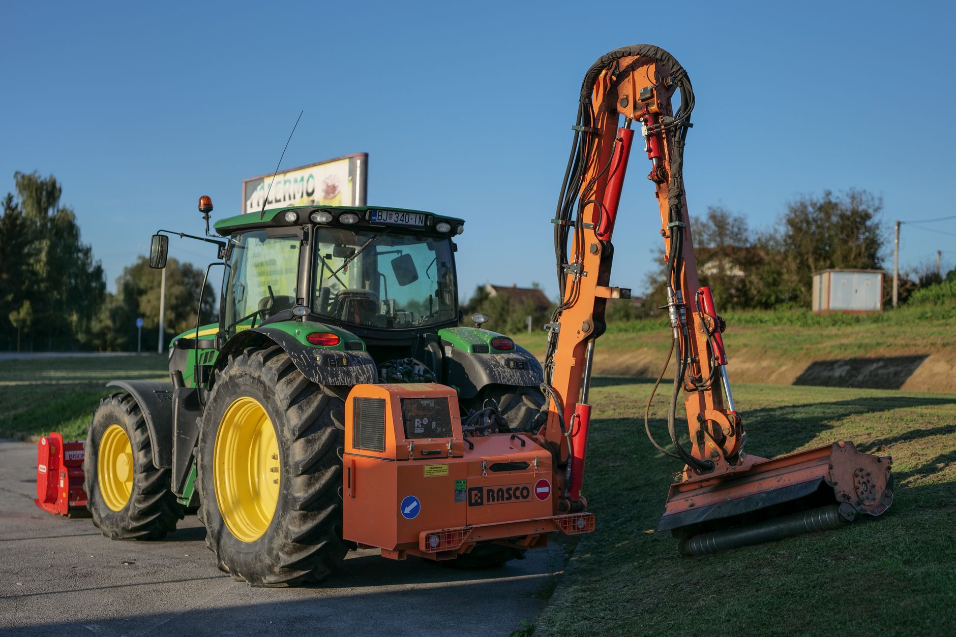 Tractor with mower attachment maintaining grass in rural Garešnica, Croatia under clear skies.