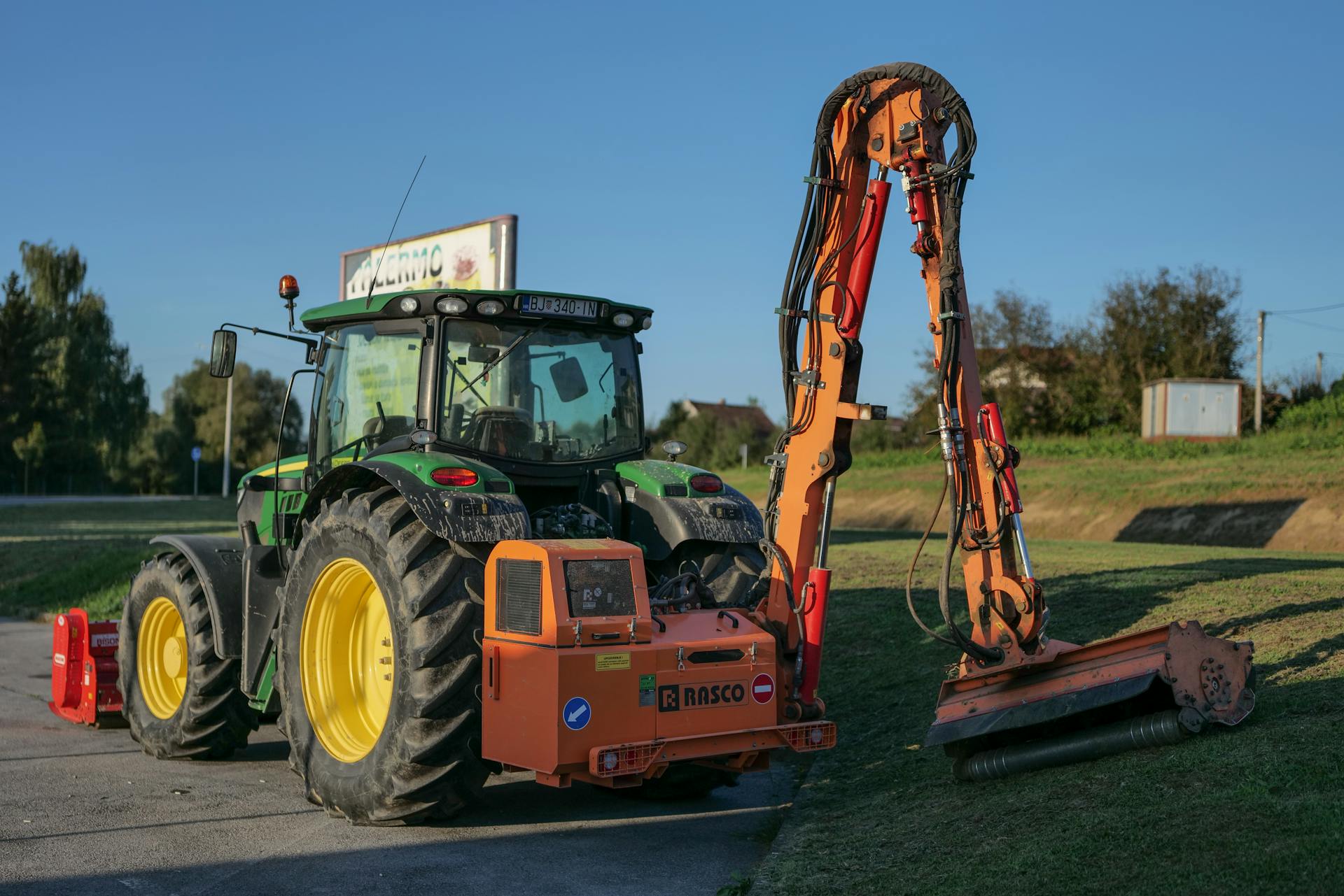 Tractor with mower attachment maintaining grass in rural Garešnica, Croatia under clear skies.