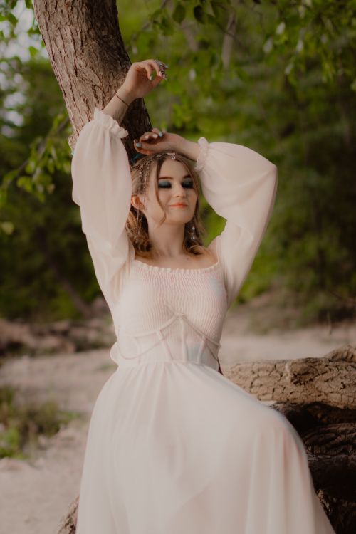 Free A serene woman in a white dress enjoys nature, eyes closed, under a tree. Stock Photo