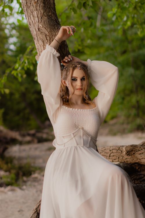 Free Elegant woman in a vintage-style wedding dress posing outdoors by a tree, radiating a serene and sophisticated aura. Stock Photo