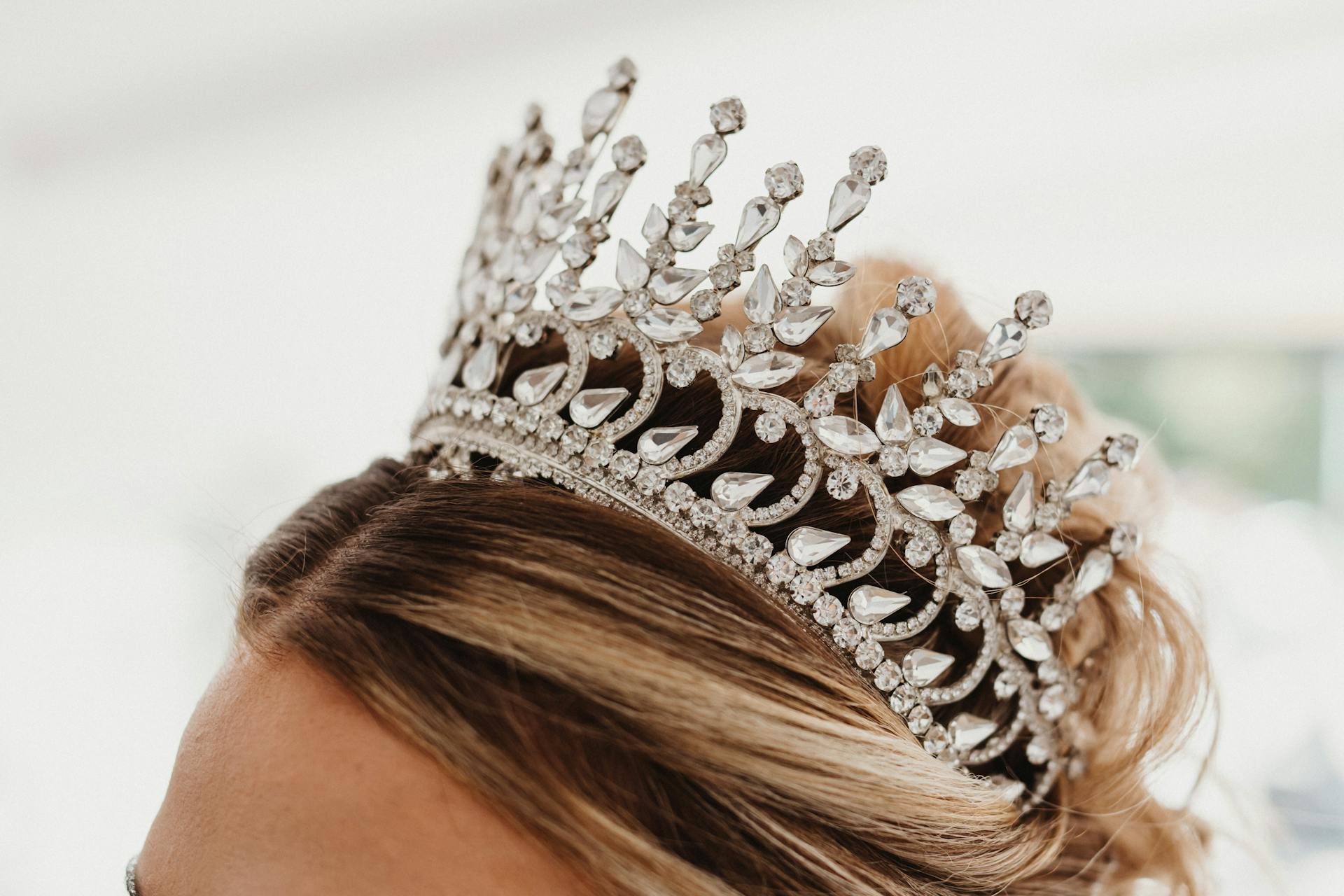 Close-up of a sparkling crystal tiara worn on blonde hair, exuding elegance and luxury.