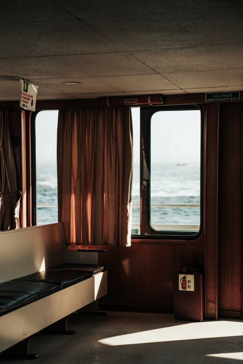 Free Warm sunlight filters through ferry windows highlighting seating area on a calm sea journey. Stock Photo