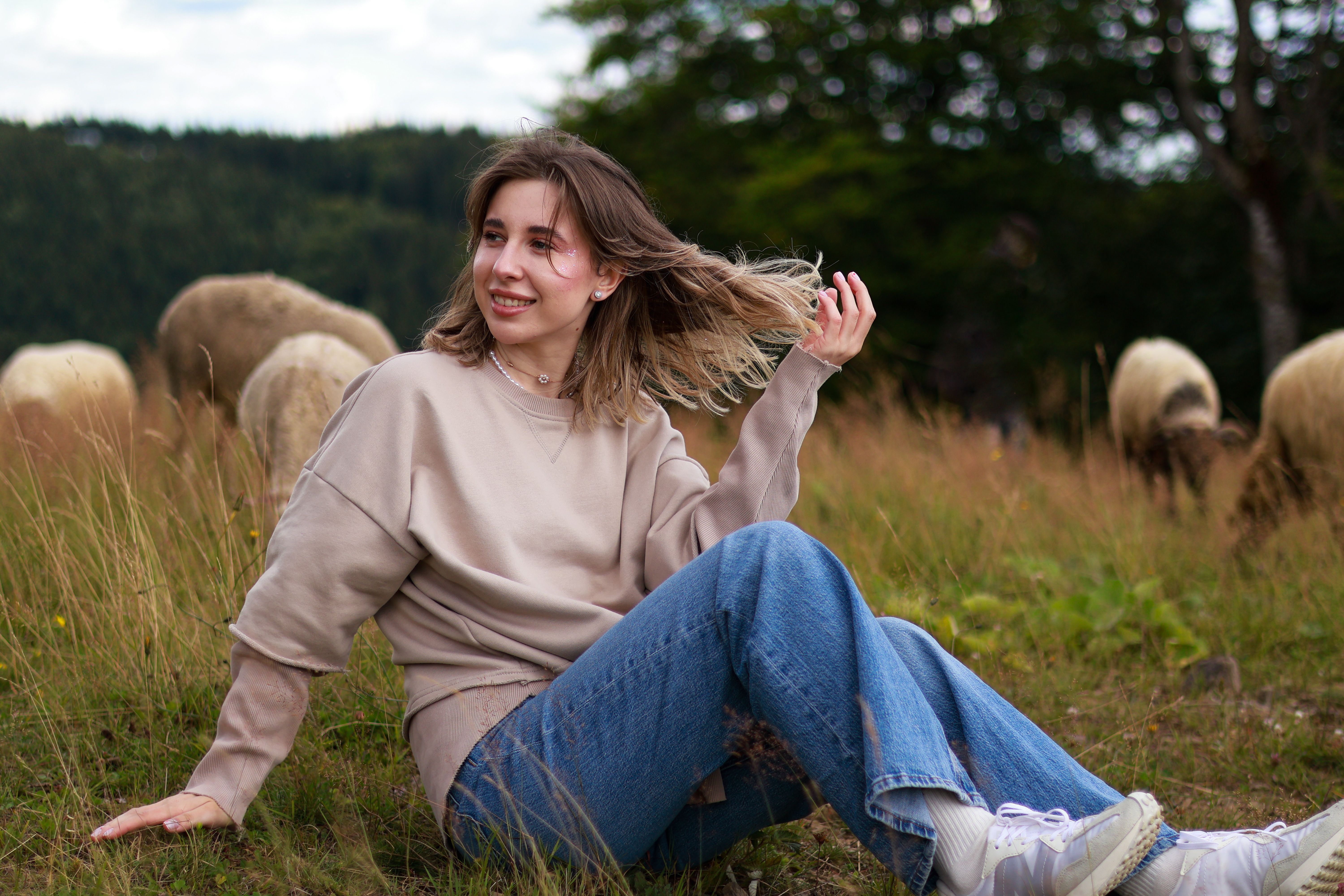 Femme en pull beige oversize et jean assis dans un champ naturel décontracté