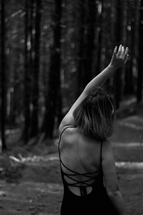 Grayscale Photo of a Woman Standing with an Arm Raised in the Forest