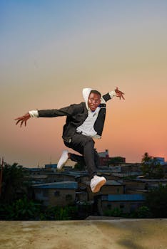 Dynamic fashion photo of a man jumping midair on a rooftop during a vibrant sunset.