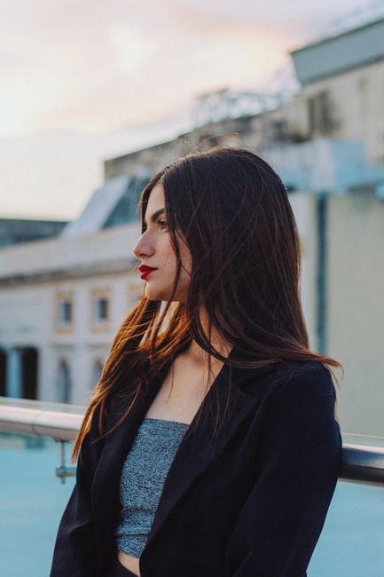 Young woman in fashionable attire poses against an urban backdrop at sunset.